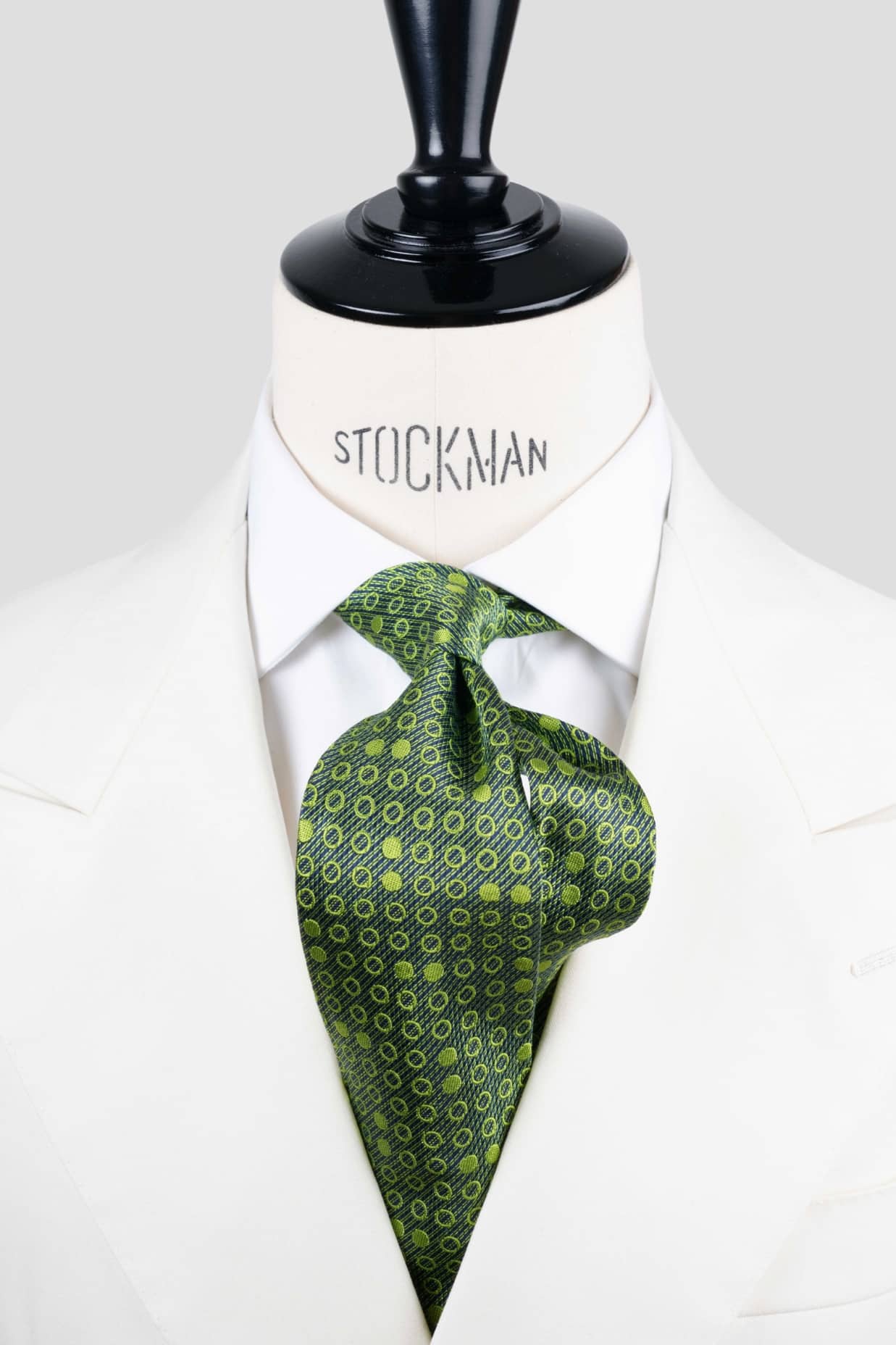Cravate sartoriale à 7 plis, en soie tissée Jacquard verte, motif rond et aperçu du noeud simple sur buste Stockman.
